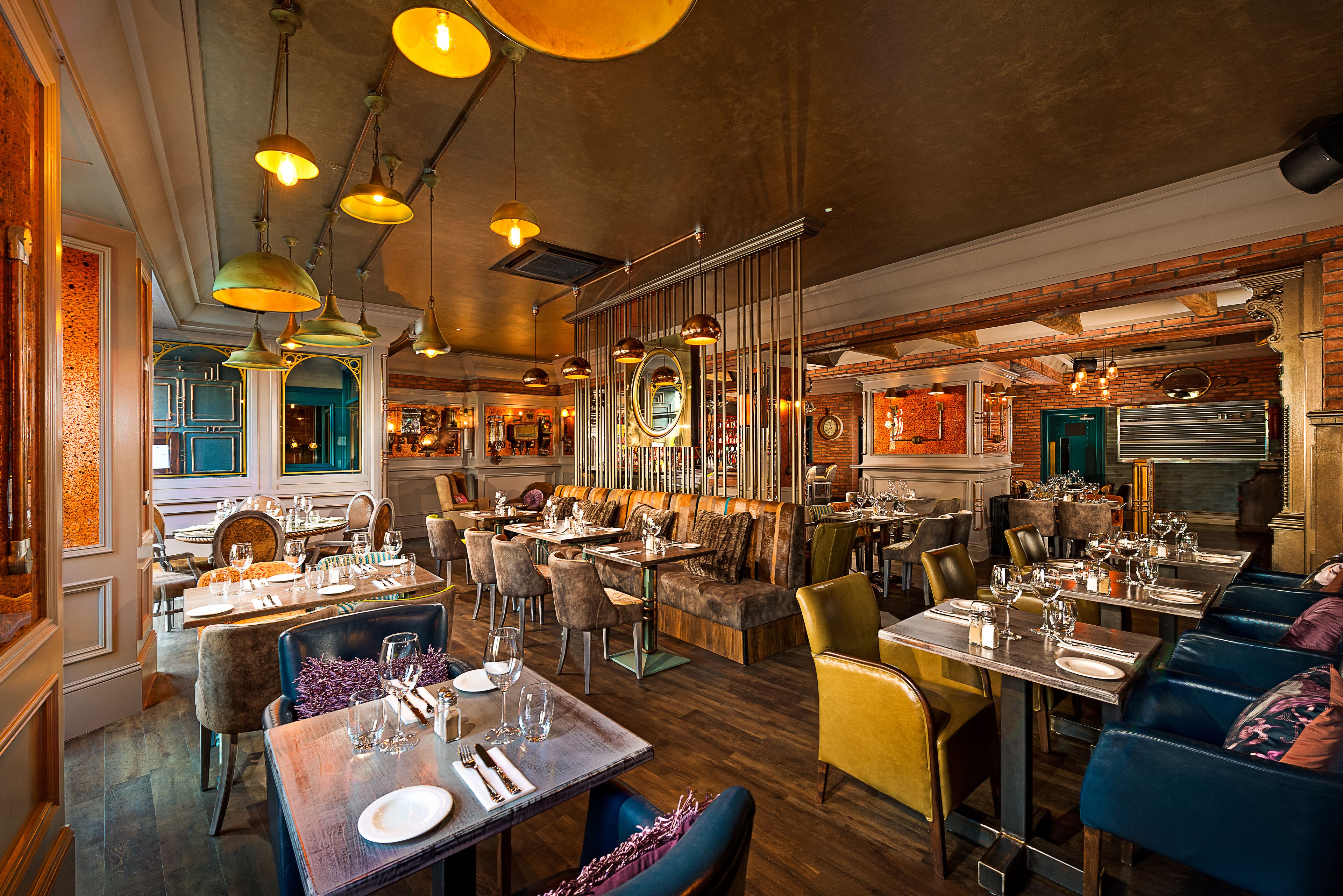A restaurant with multiple dining areas, including booths and tables, with hanging pendant lights and brick walls.