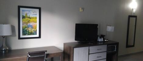 A hotel room with a desk, chair, television, and a bed.