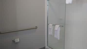 Un baño con cabina de ducha de vidrio, inodoro y pasamanos.