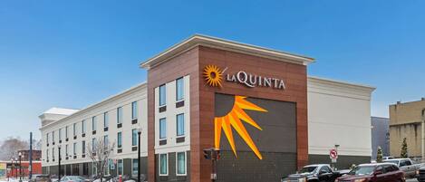 A hotel with a large sun logo on the facade, multiple windows, and a parking lot with cars.