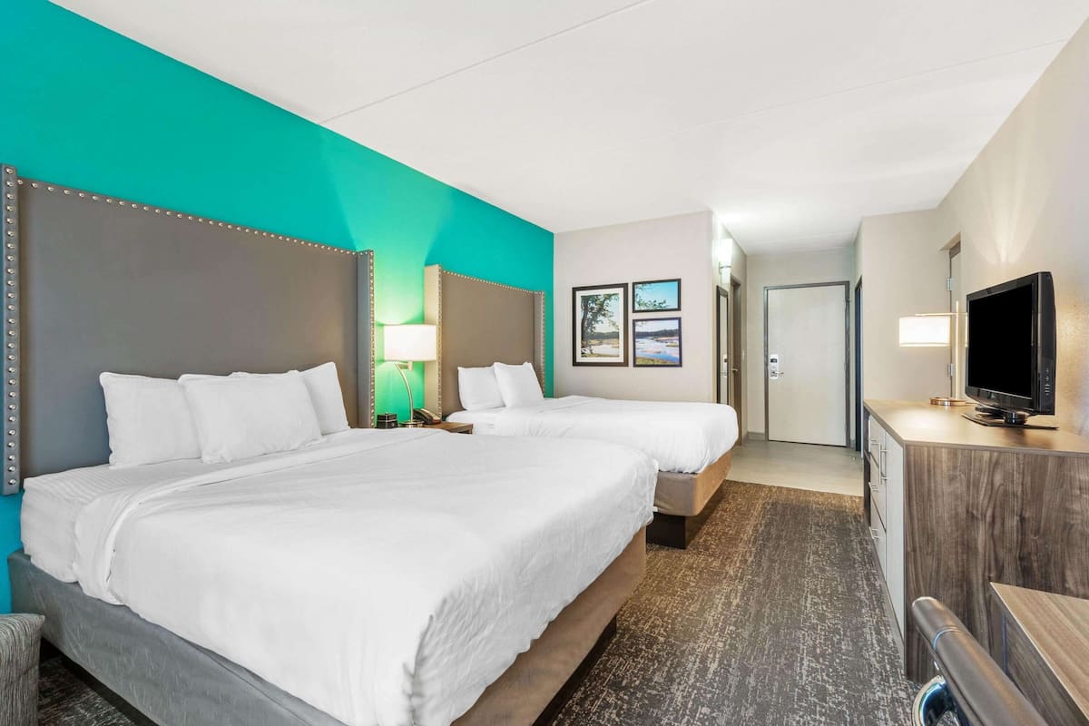 A hotel room with two beds, a TV, and a desk.