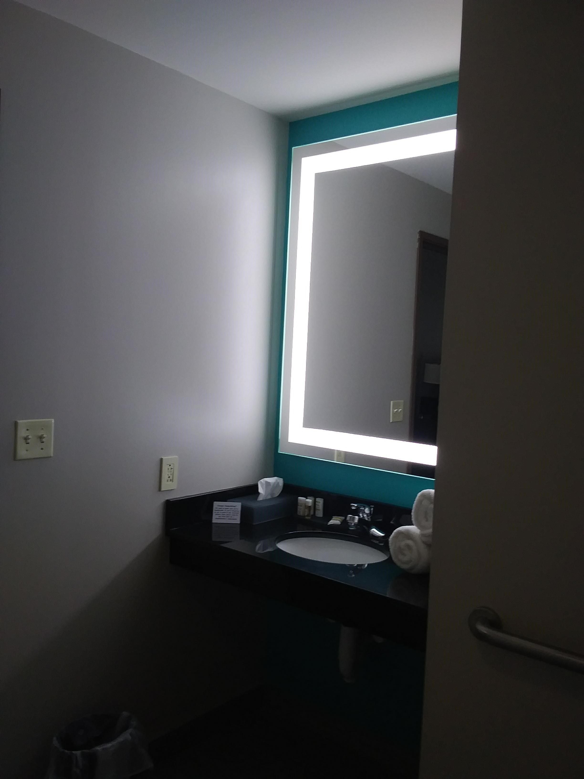 Une salle de bain avec un lavabo noir, un miroir avec un cadre turquoise et une serviette blanche posée sur le comptoir.