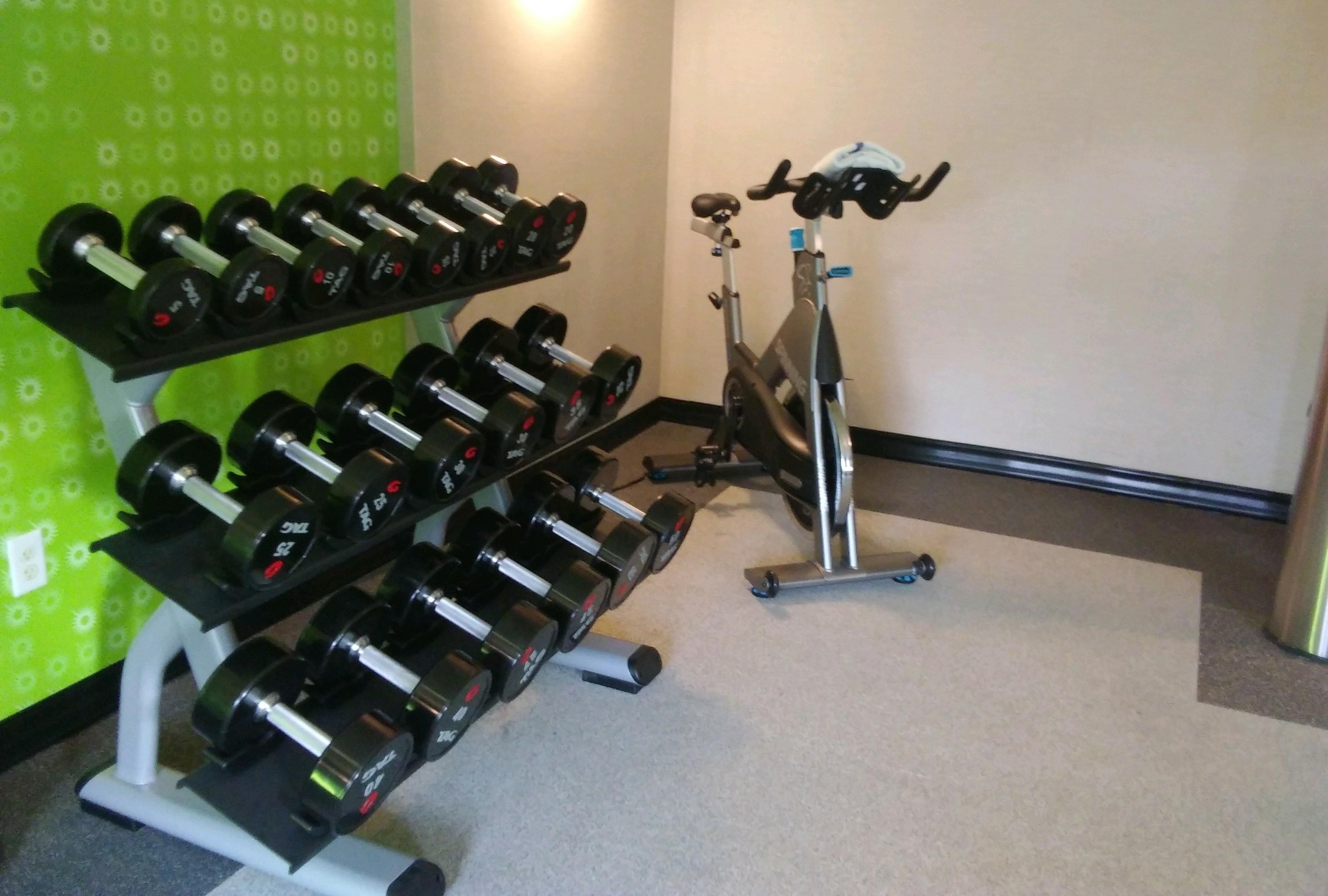 A gym with a stationary bike and a rack of dumbbells.