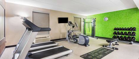 A gym with treadmills, a stationary bike, a weight bench, and a wall-mounted dumbbell rack.