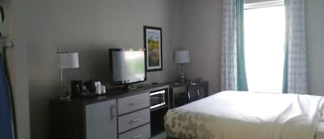 Una habitación de hotel con cama, televisor, escritorio con lámpara y ventana con cortinas.