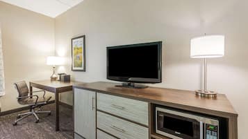 A hotel room with a wooden desk, a flat-screen TV, a lamp, a microwave, and a chair.