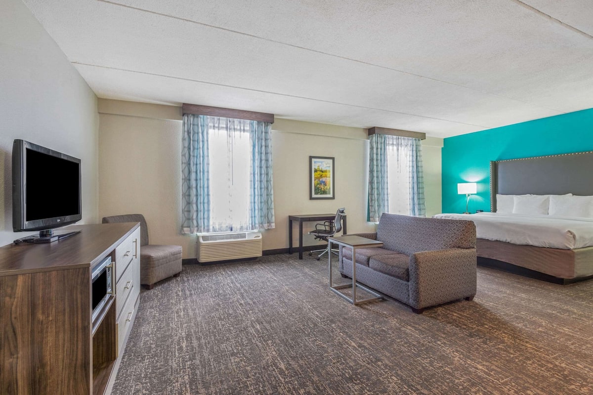A hotel room with a bed, a desk, a television, a chair, and a small table.