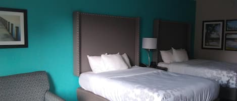 Een hotelkamer met twee bedden, een grijze fauteuil en een kleine tafel.