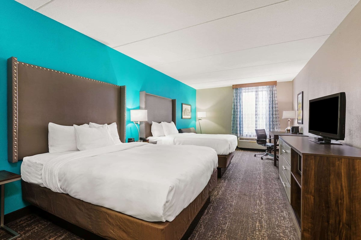 A hotel room with two beds, a desk, a TV, and a window with curtains.