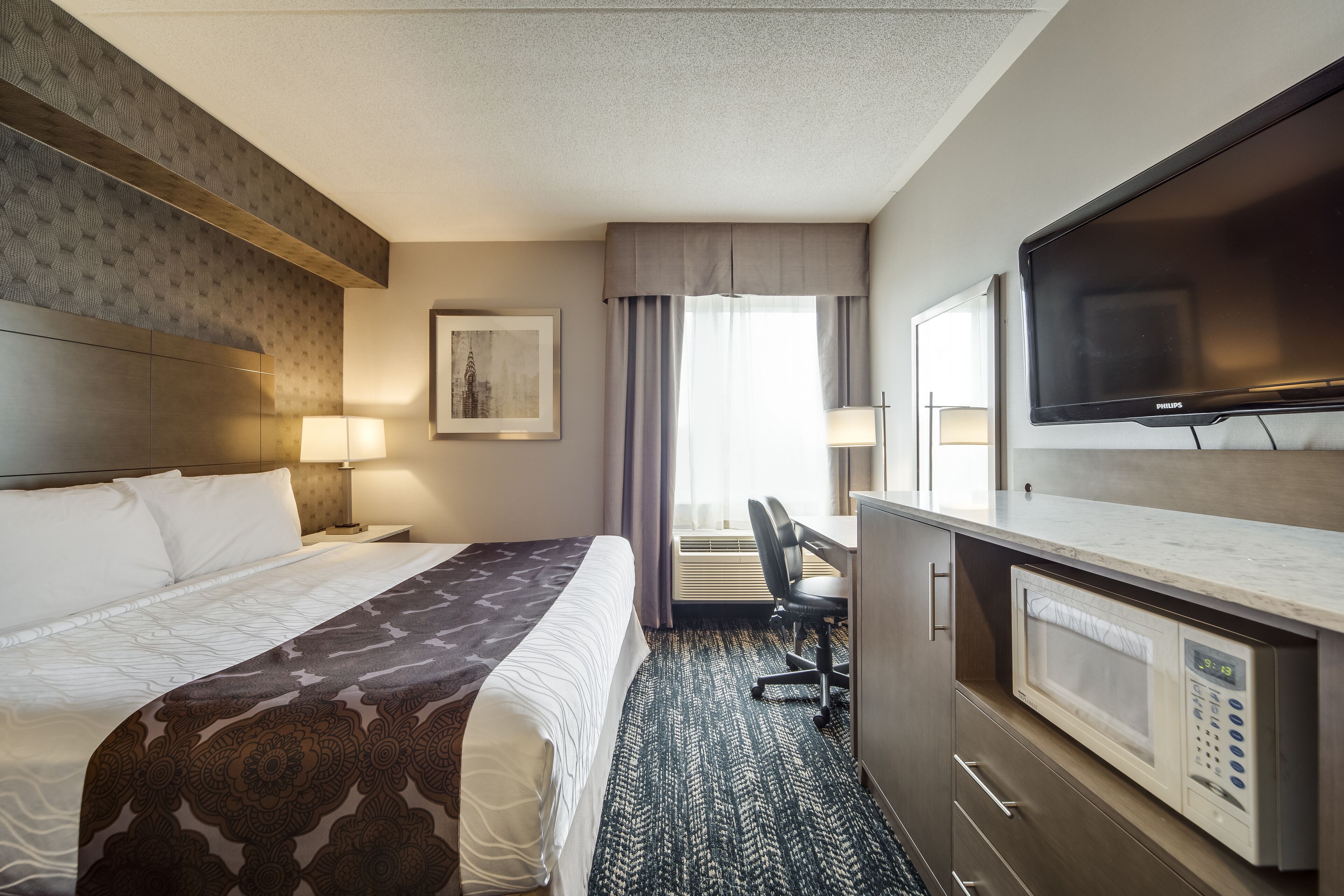 A hotel room with a bed, desk, chair, television, and microwave.