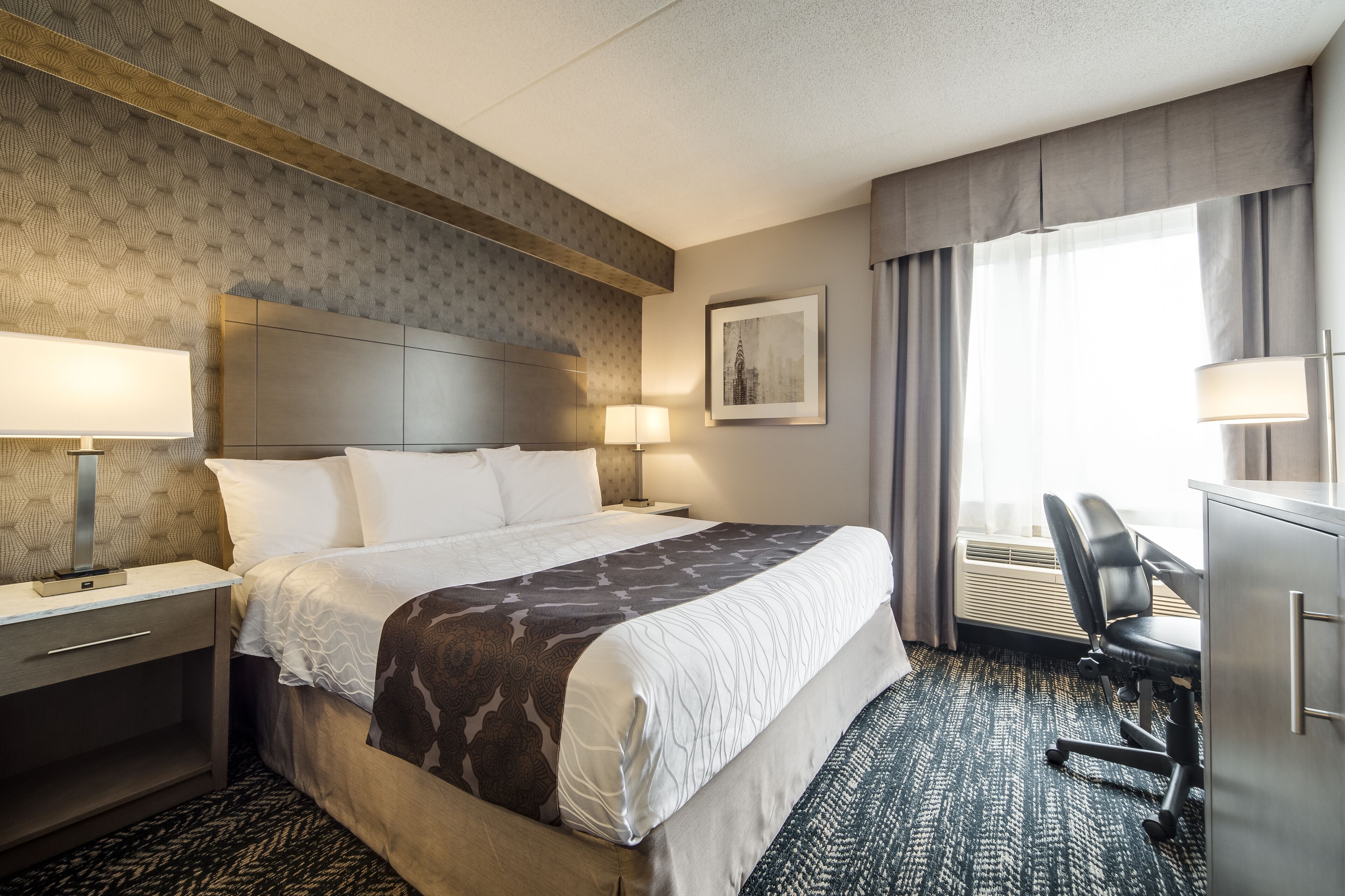 Ein Hotelzimmer mit einem großen Bett, Nachttischen, einem Schreibtisch und einem Sessel.