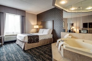 A hotel room with a bed, a large mirror, a bathtub, and a window with curtains. - Monte Carlo Inn - Brampton Suites (Brampton)