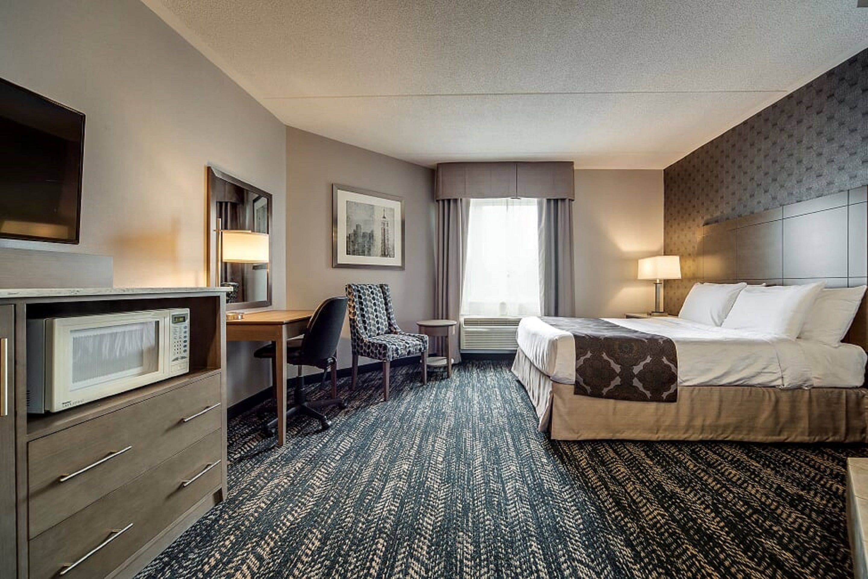 A hotel room with a bed, desk, chair, and a microwave.