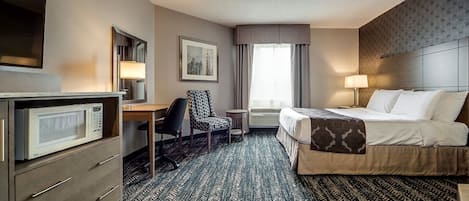 A hotel room with a bed, desk, chair, and a microwave.