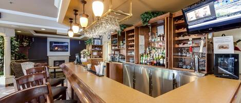 Uma área de bar com cadeiras de madeira, balcão e uma tela de televisão exibindo notícias.
