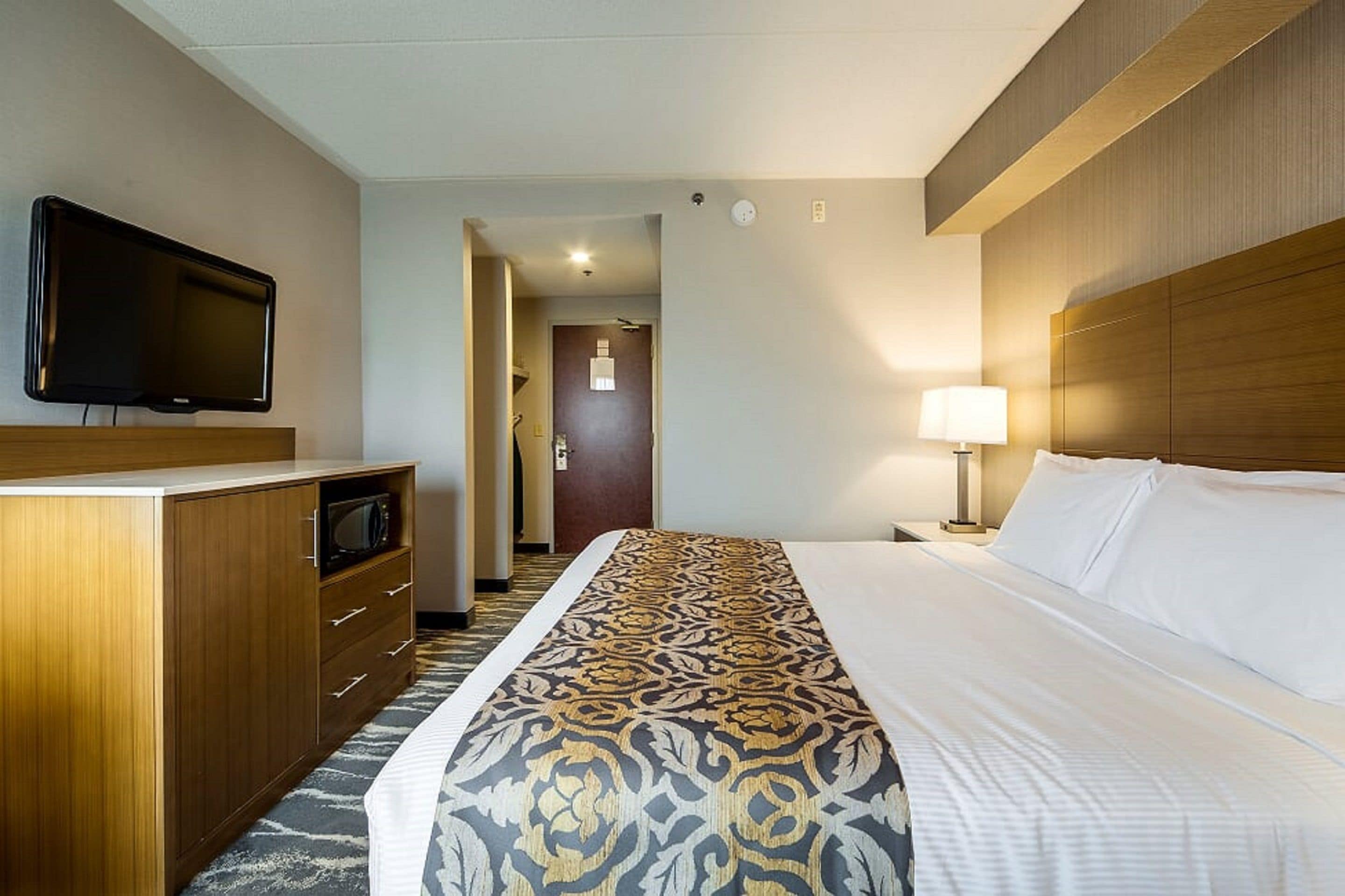 Une chambre d’hôtel comprenant un lit, une télévision, un bureau avec un micro-ondes et une porte donnant sur une autre pièce.
