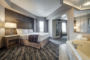 A hotel room with a bed, nightstand, lamp, and a large bathtub.