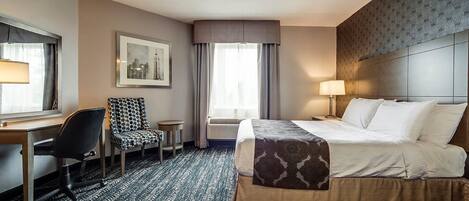 A hotel room with a bed, desk, chair, and a window with curtains.