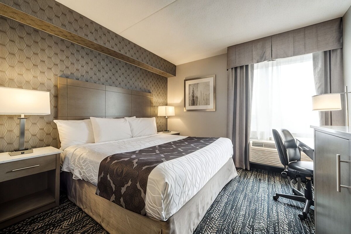 A hotel room with a large bed, bedside lamps, a desk with a chair, and a window with curtains.