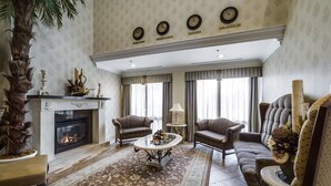 A spacious living room with a fireplace, comfortable seating, and a large window with curtains. - Monte Carlo Inn - Brampton Suites (Brampton)