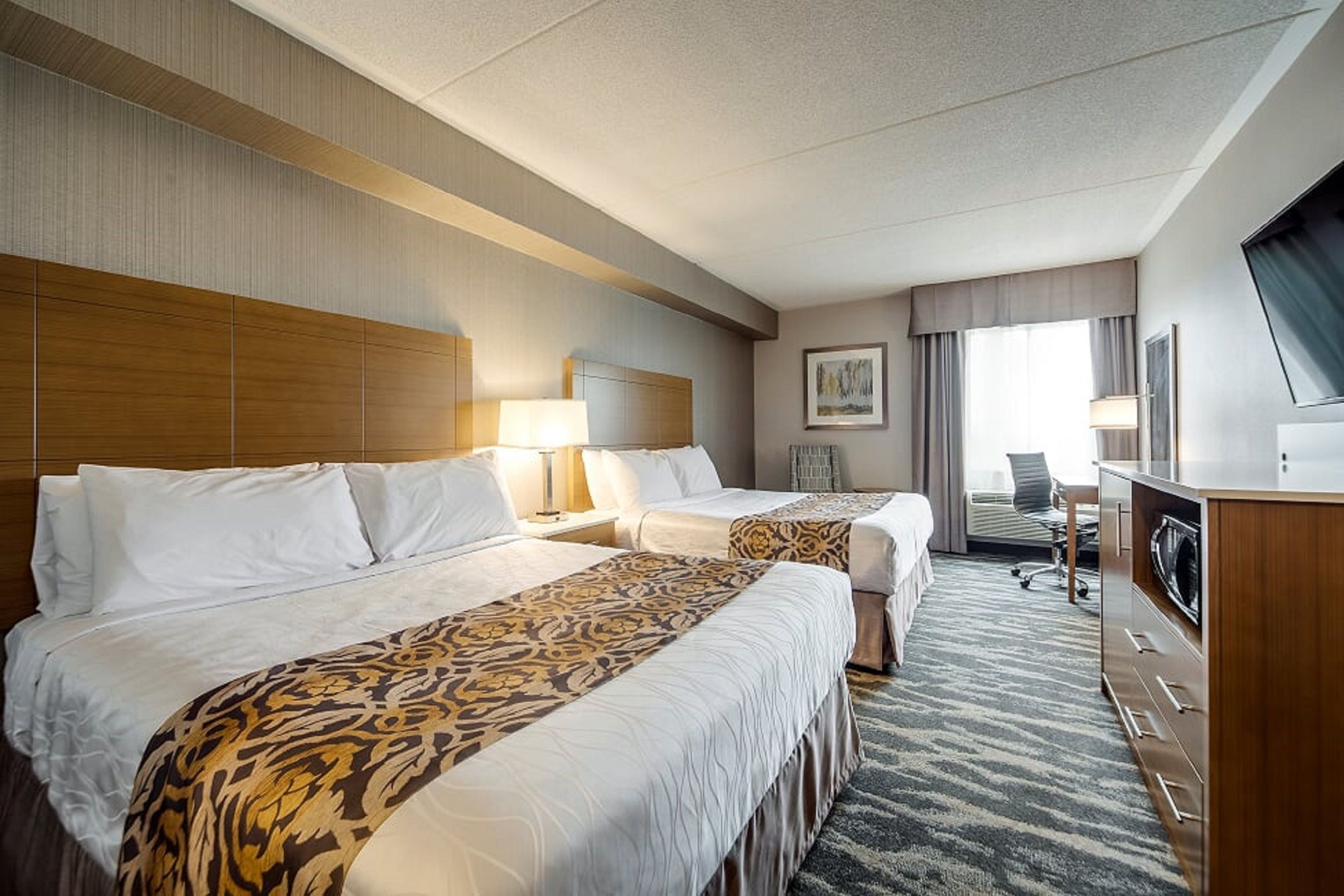 A hotel room with two beds, a desk, a chair, a TV, and a window with curtains.