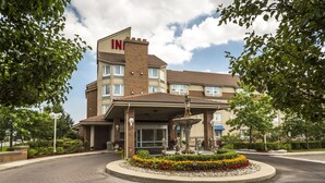 A hotel entrance with a fountain, brick pathway, and a landscaped garden. - Monte Carlo Inn - Brampton Suites (Brampton)