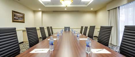 A conference room with a long table, black chairs, water bottles, and a chandelier.