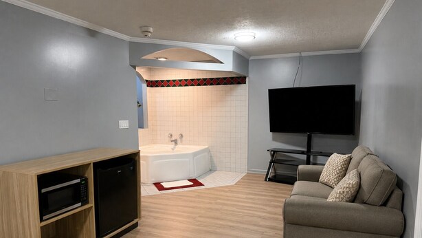 Ein modernes Wohnzimmer mit Flachbildfernseher, einer Couch, einem Holzschrank mit Mikrowelle und einem Badezimmer mit Badewanne.
