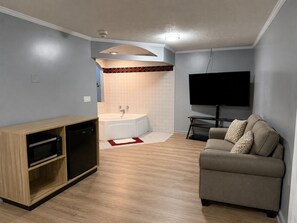 Una sala de estar moderna con un televisor de pantalla plana, un sofá, un mueble de madera con microondas y un baño con bañera.