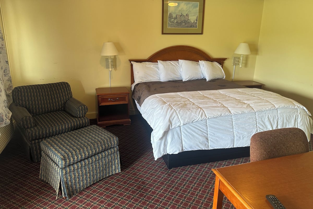 A hotel room with a bed, a chair, a table, and a nightstand.