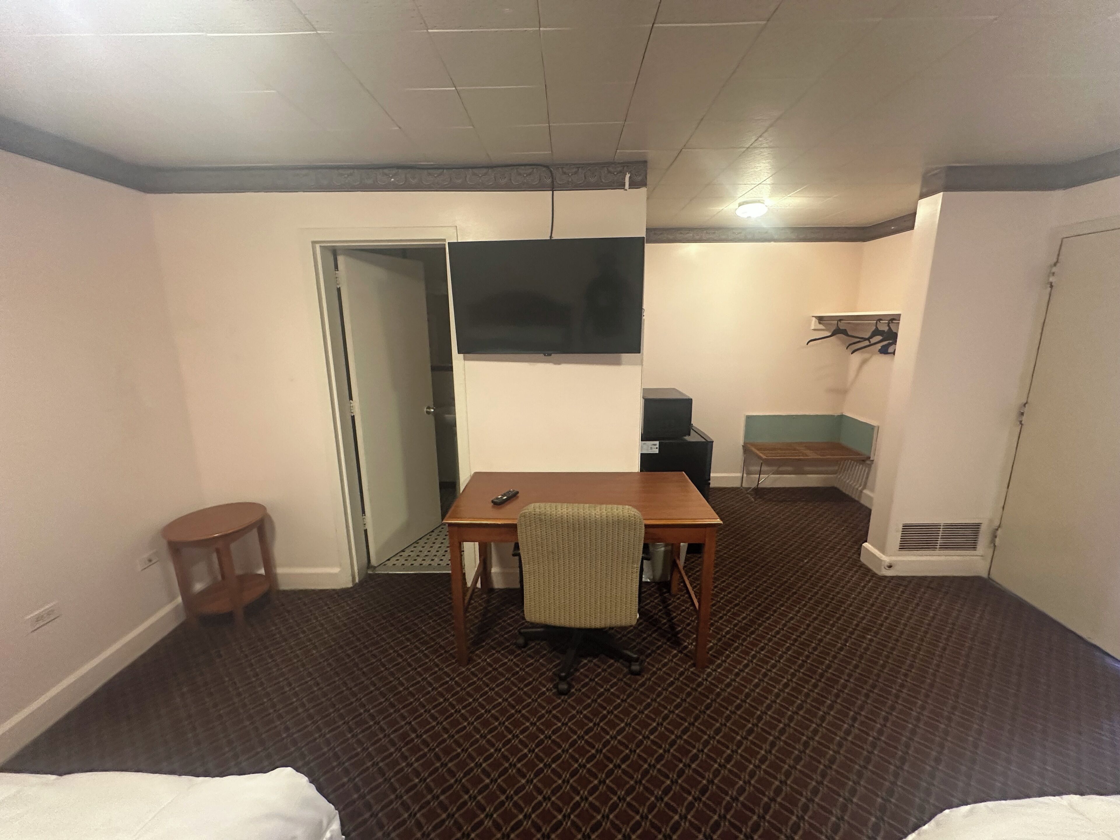 A hotel room with a bed, a desk, a chair, a television, a small table, and a coat rack.