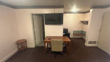 A hotel room with a bed, a desk, a chair, a television, a small table, and a coat rack.