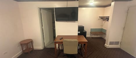 A hotel room with a bed, a desk, a chair, a television, a small table, and a coat rack.