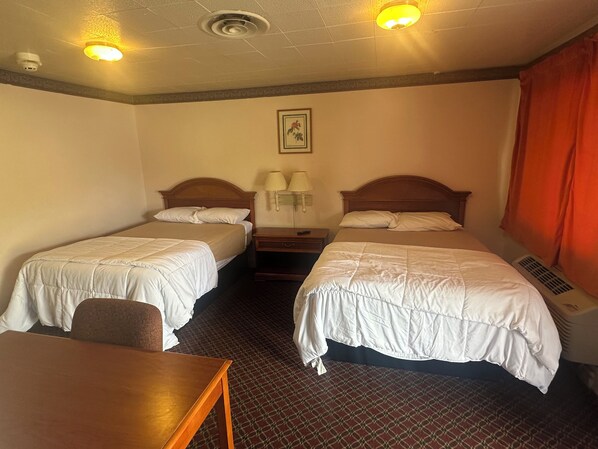 Habitación de hotel con dos camas, un escritorio, una mesita de noche, una lámpara, un cuadro en la pared y una ventana con cortinas.