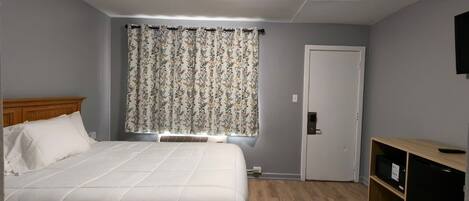 A bedroom with a bed, a window with curtains, a door, and a TV mounted on the wall.