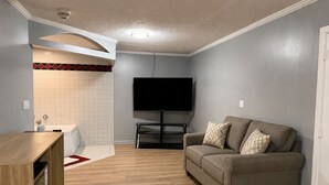 Ein Wohnzimmer mit Flachbildfernseher, einer Couch, einem Holzschrank und einem gefliesten Duschbereich.