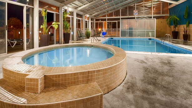 A large indoor swimming pool with a hot tub, surrounded by glass doors and potted plants. - Sandcastle Resort On The Beach (Virginia Beach)