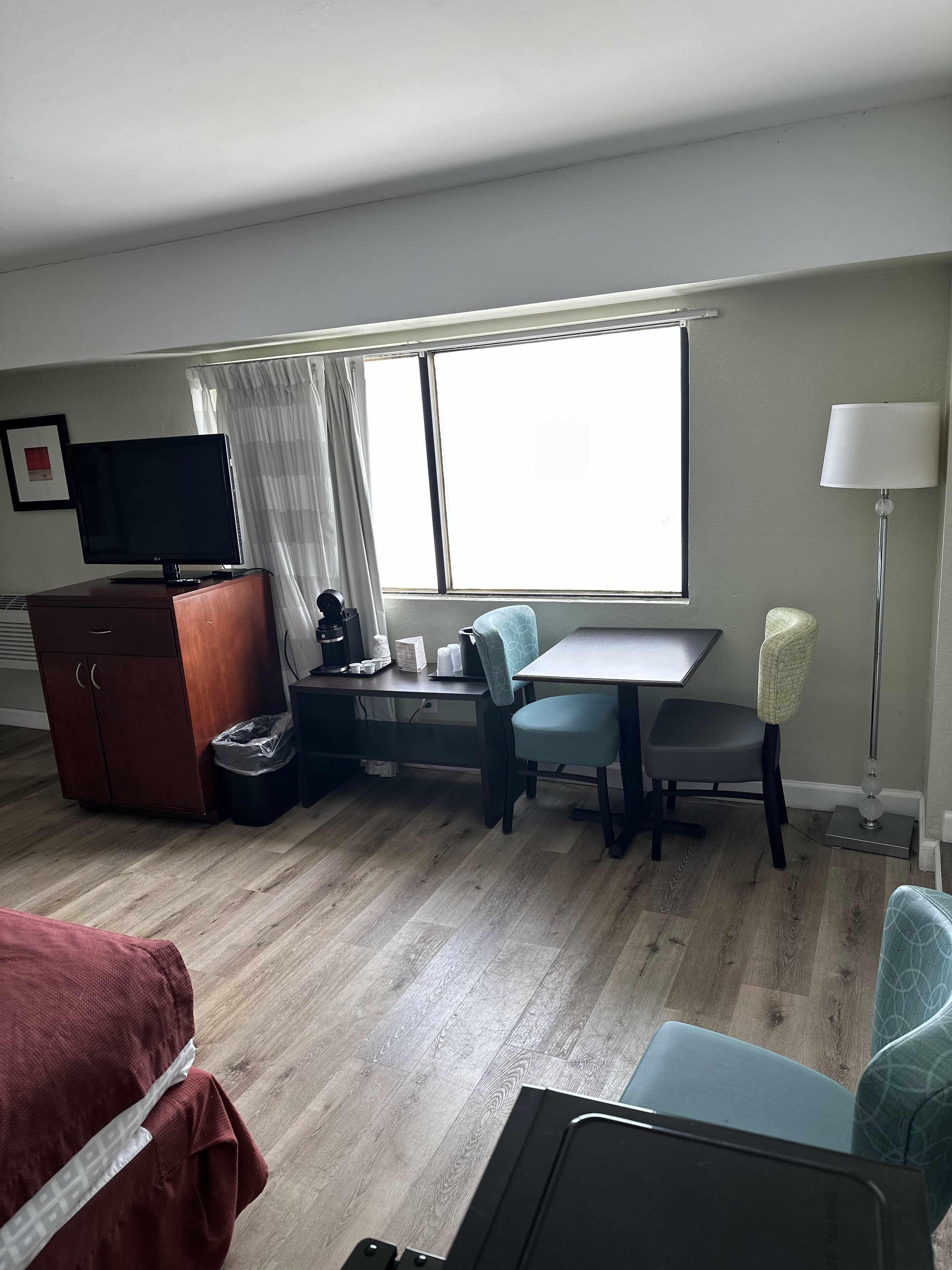Habitación de hotel con cama, escritorio, silla, televisor, lámpara y ventana.