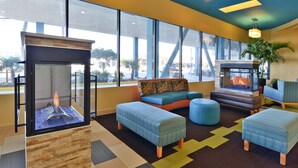A modern lobby with a fireplace, comfortable seating, and large windows. - Sandcastle Resort On The Beach (Virginia Beach)