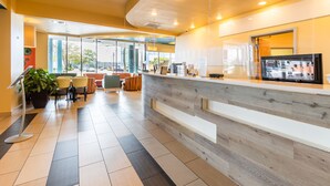 A modern reception area with a wooden reception desk, seating area, and large windows. - Sandcastle Resort On The Beach (Virginia Beach)