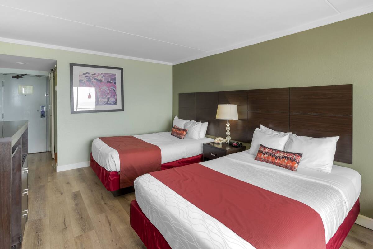 Una habitación de hotel con dos camas, un cabecero de madera, una mesita de noche con lámpara y un cuadro en la pared.