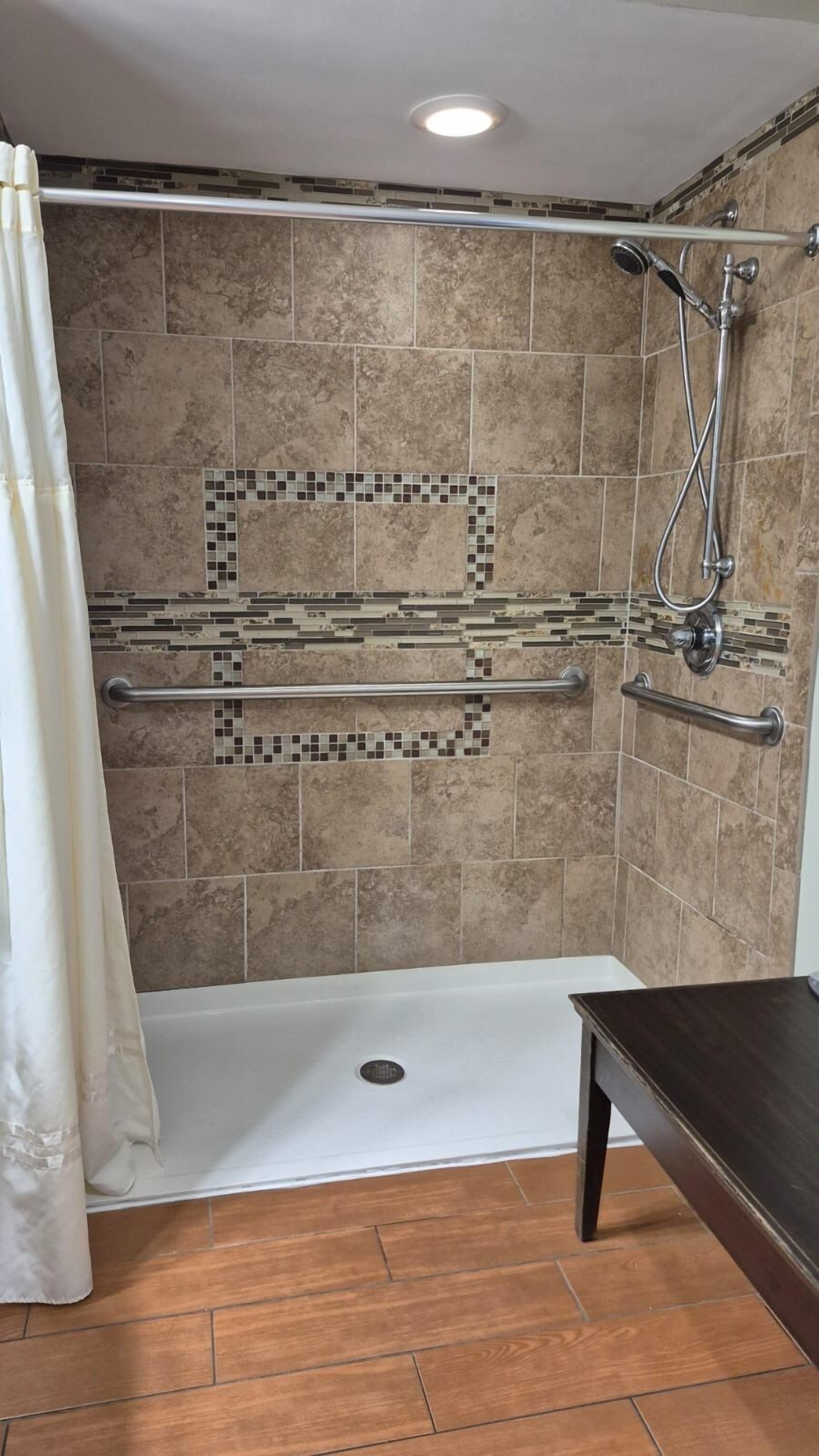 A shower area with a tiled wall, a grab bar, and a showerhead.