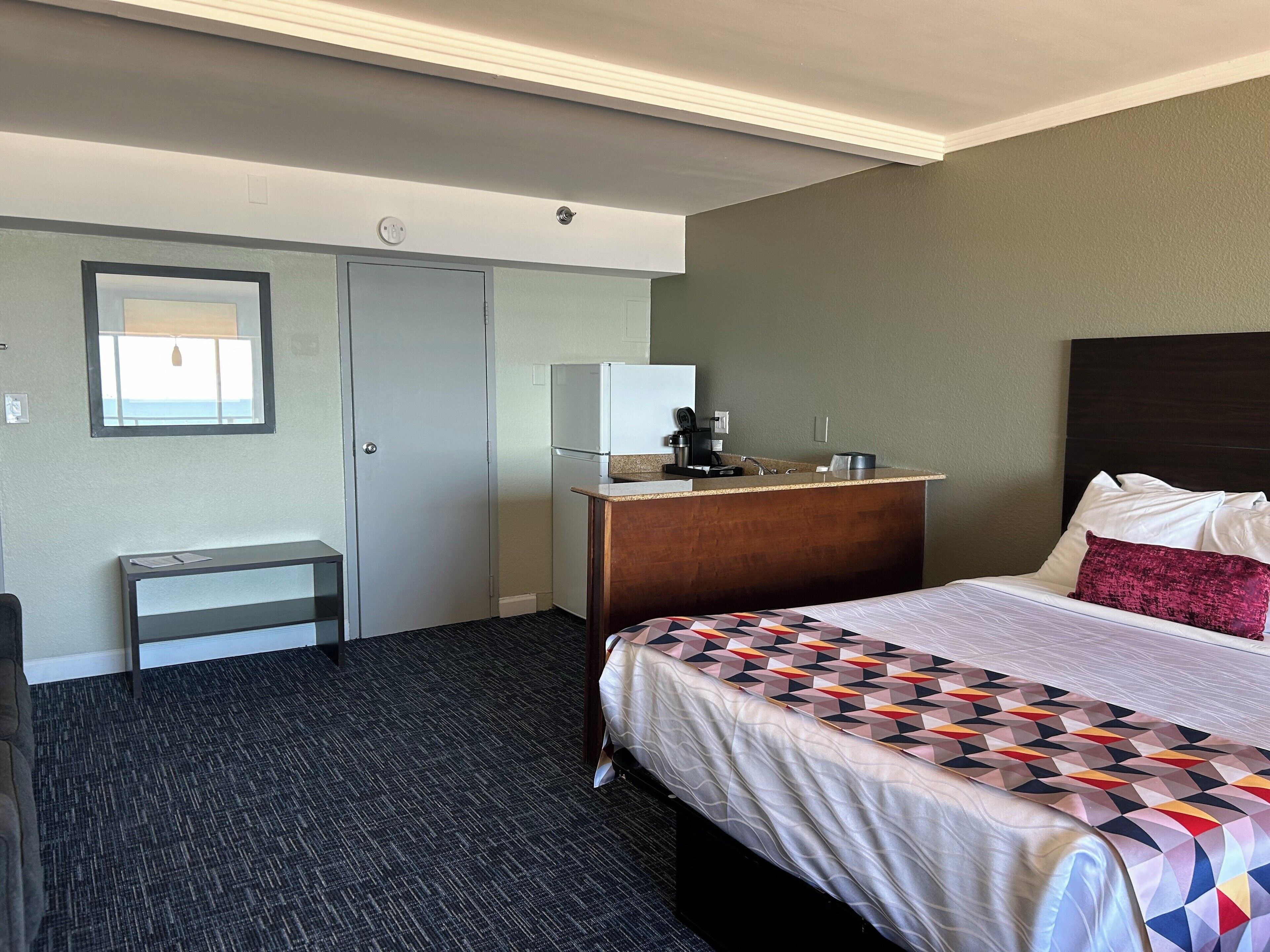 Une chambre d’hôtel avec un lit, un bureau, une petite kitchenette et une fenêtre.