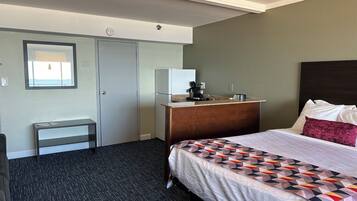 A hotel room with a bed, a desk, a small kitchenette, and a window.