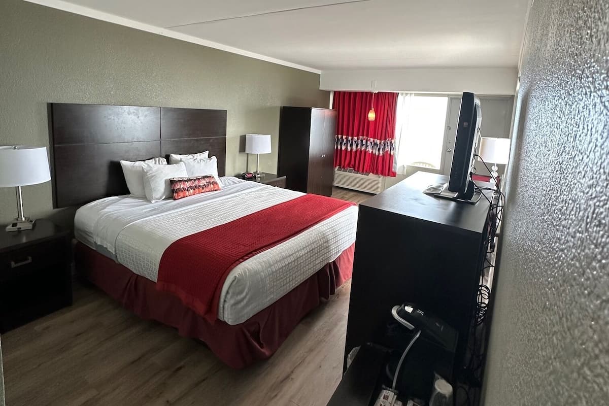 Una habitación de hotel con una cama, un escritorio, un televisor y un zapatero.
