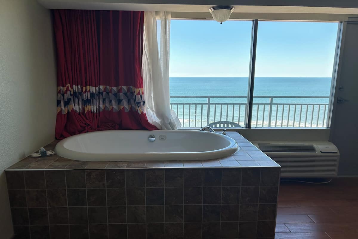 Un baño con una bañera grande, una ventana con vistas al mar y una lámpara en el techo.