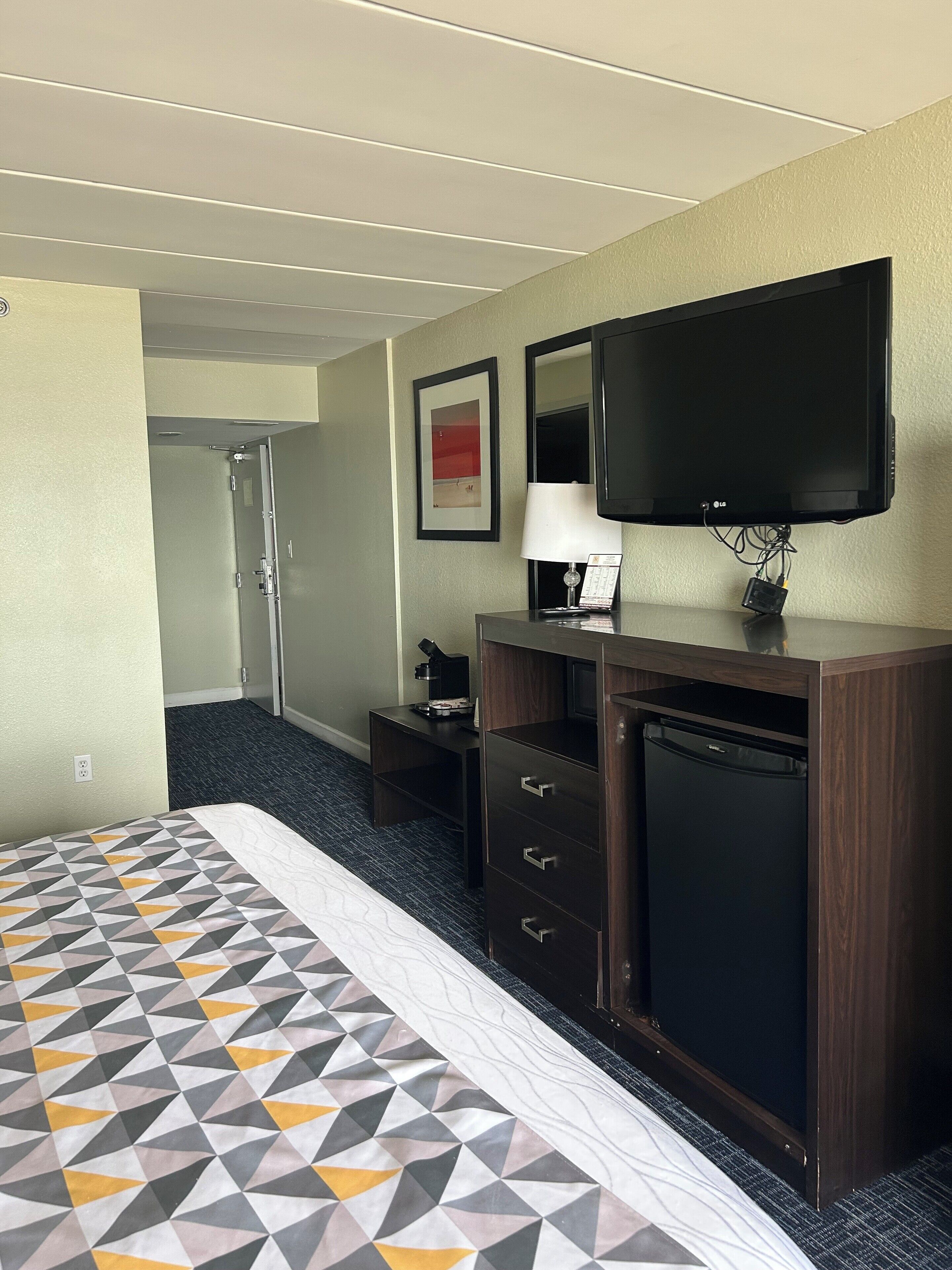 A hotel room with a bed, a desk, a television, a lamp, and a refrigerator.
