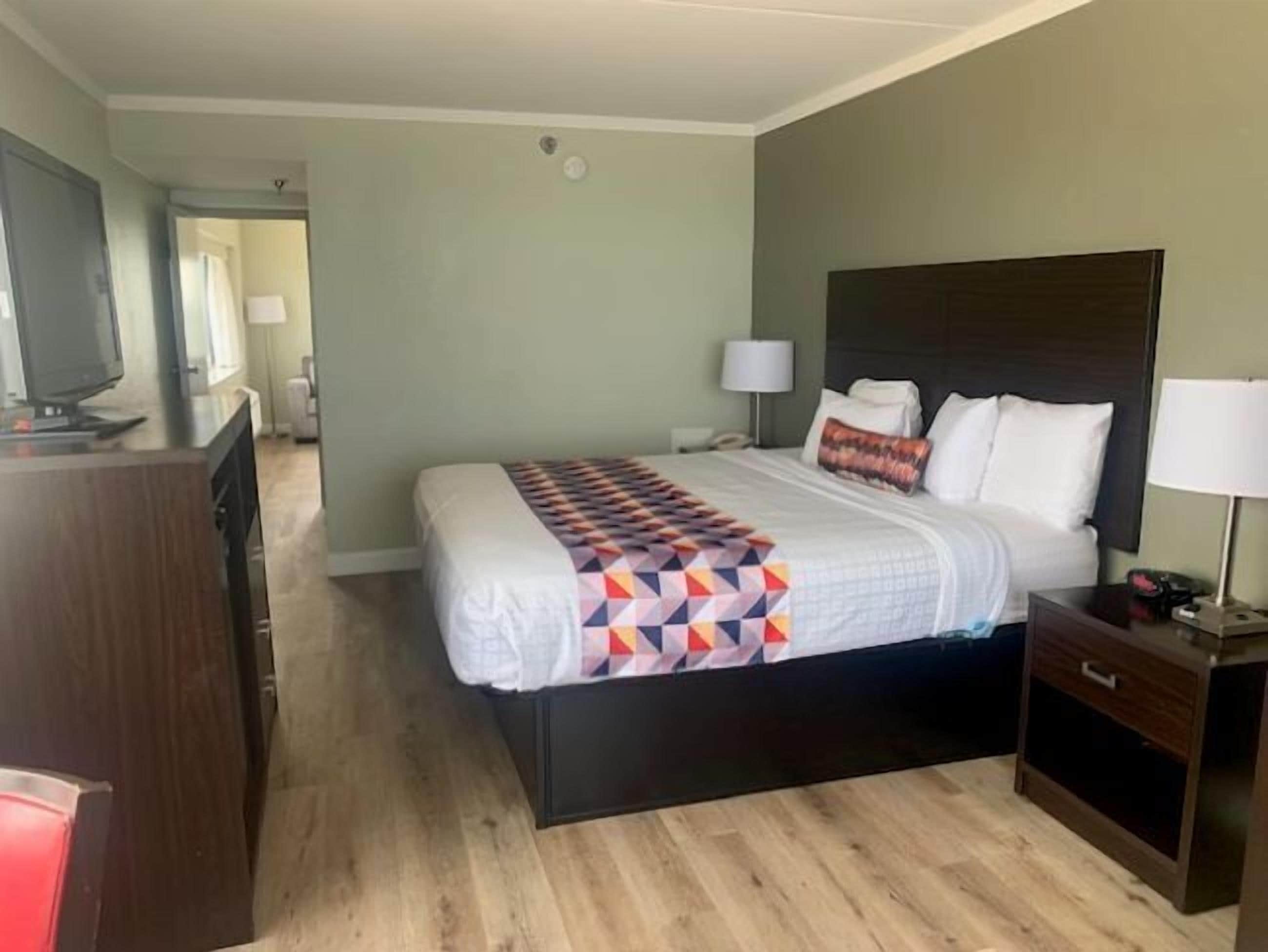 A hotel room with a bed, bedside tables, a TV, and a desk.