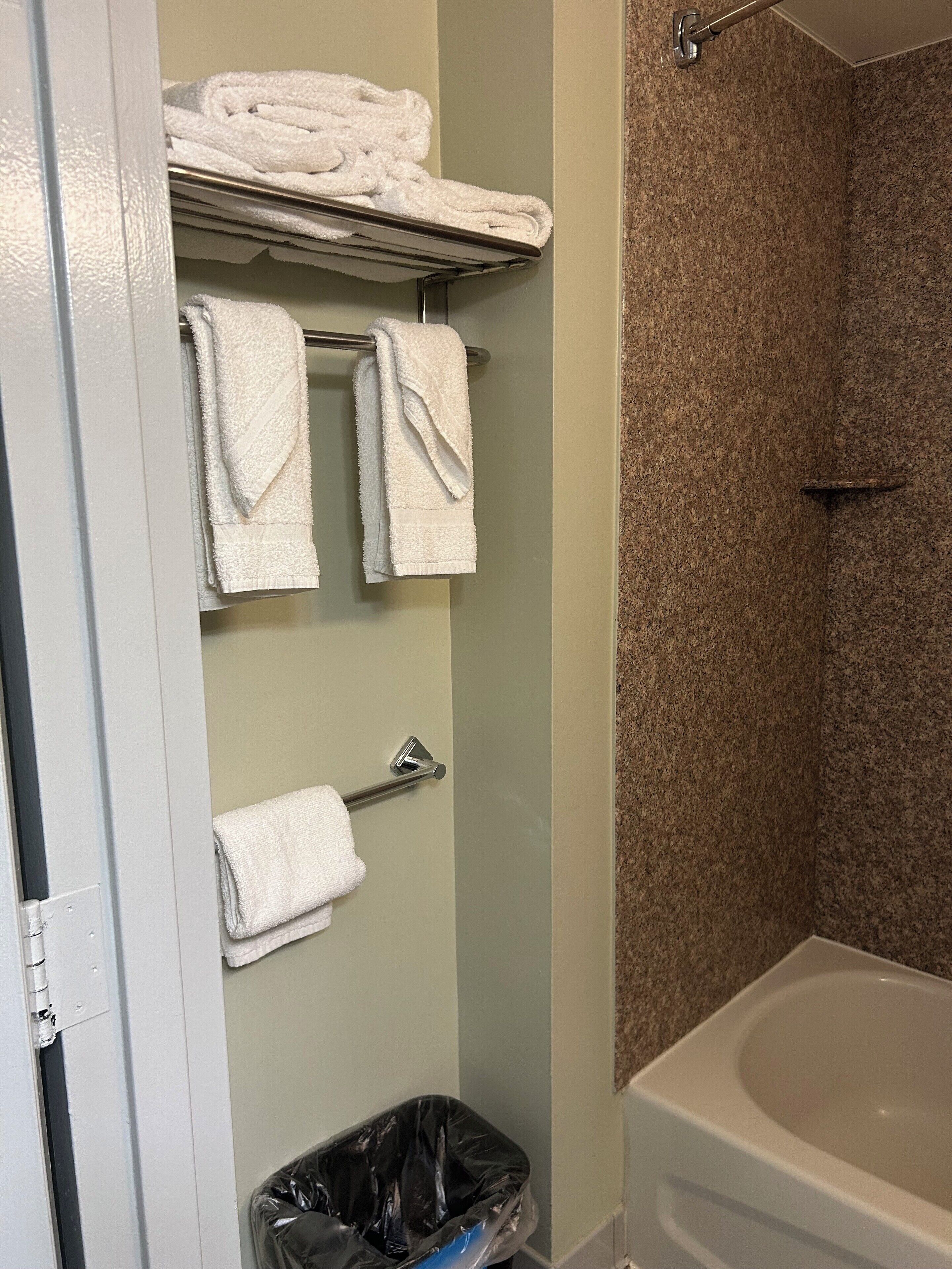 A bathroom with a bathtub, a towel rack with folded towels, and a trash bin.
