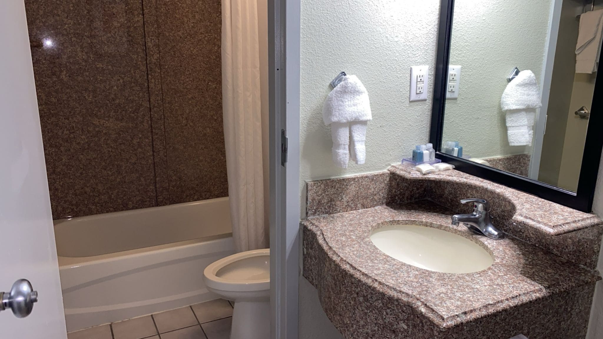 A bathroom with a granite sink, a mirror, a toilet, and a shower area.